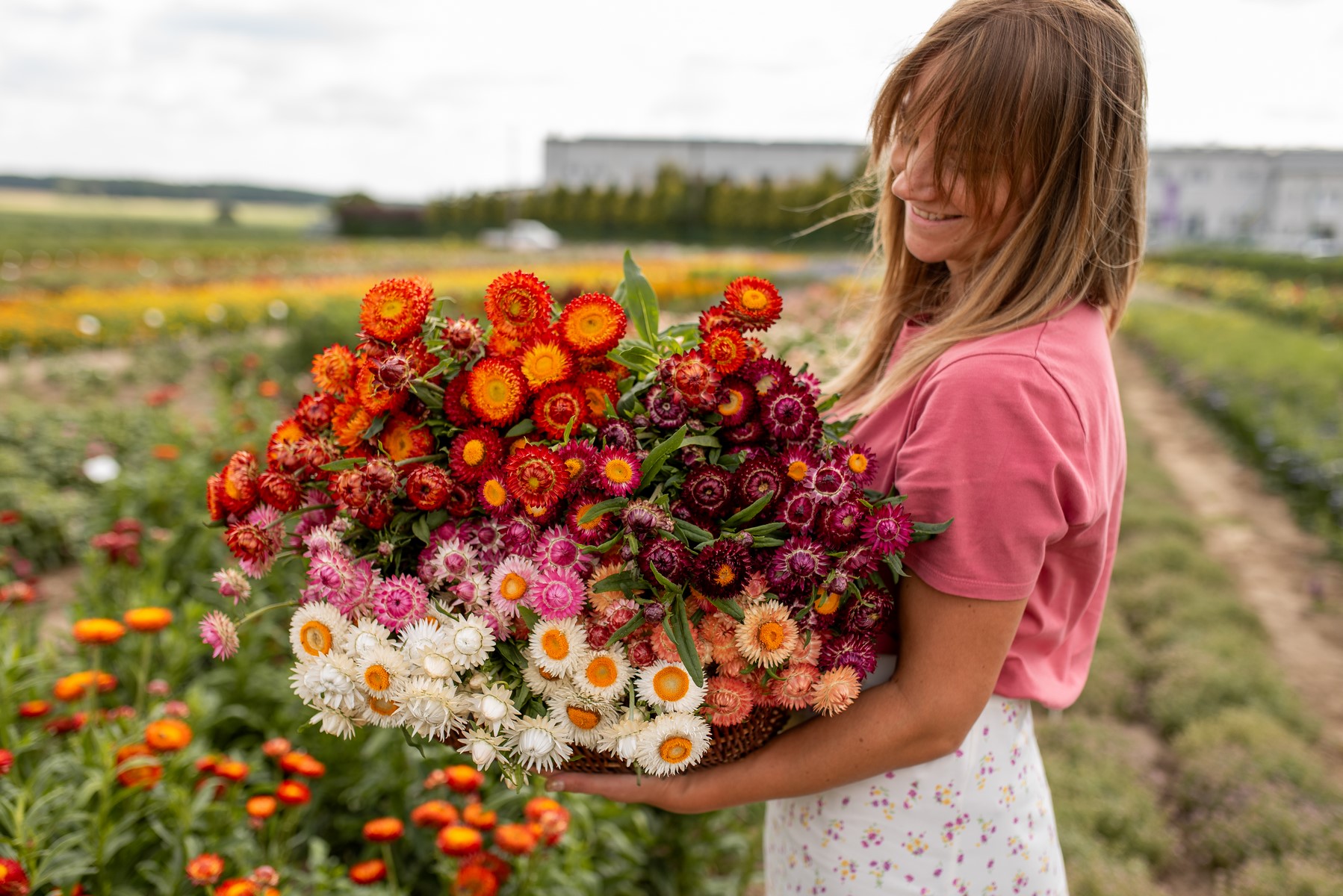 dziewczyna w różowej bluzce stoi na polu z koszem pełnym kolorowych kocanek